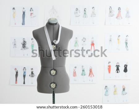 professional dressmakers dummy with measuring tape, with fashion sketches on wall behind