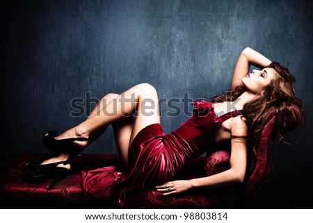 elegant sensual young woman in red dress on recamier indoor shot - stock photo