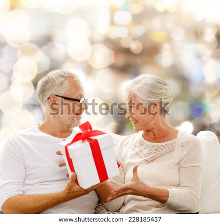 family, holidays, christmas, age and people concept - happy senior couple with gift box over lights background