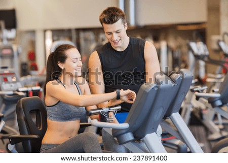 sport, fitness, lifestyle, technology and people concept - happy woman with trainer working out on exercise bike in gym