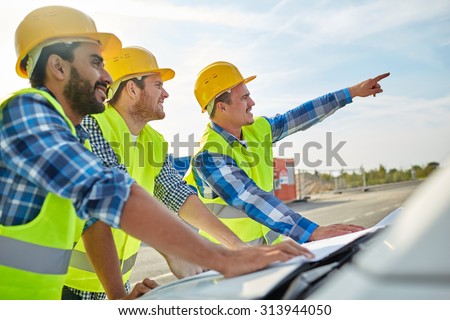 building, construction, development, teamwork and people concept - close up of builders in hardhats and high visible vests with blueprint on car hood