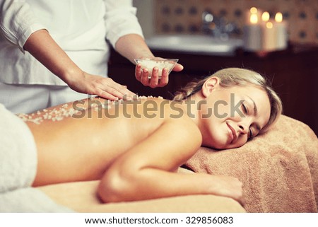 people, beauty, spa, massage and relaxation concept - close up of beautiful young woman lying with closed eyes and therapist holding salt bowl in spa