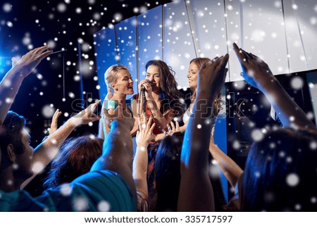 party, holidays, celebration, nightlife and people concept - happy young women singing karaoke on night club stage and snow effect