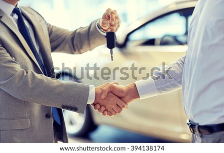 auto business, car sale, deal, gesture and people concept - close up of dealer giving key to new owner and shaking hands in auto show or salon