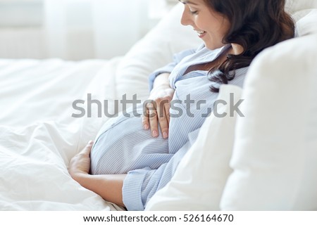 pregnancy, rest, people and expectation concept - close up of happy smiling pregnant woman lying in bed and touching her belly at home