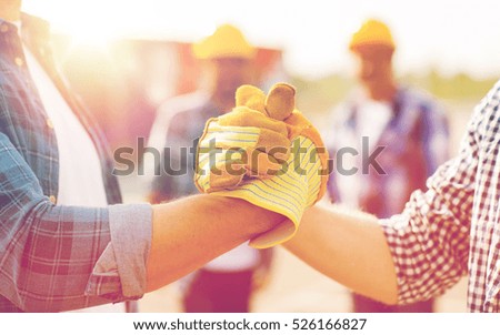 building, teamwork, partnership, gesture and people concept - close up of builders hands in gloves greeting each other with handshake on construction site