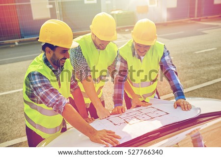 building, construction, development, teamwork and people concept - close up of builders in hardhats and high visible vests with blueprint on car hood