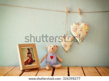 teddy bear over wood table next to photo frame with kid's old photography and fabric hearts. retro filtered image