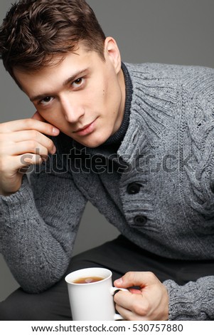 Sexy young man in warm knit sweateron with a cup of tea in his hands. Male model.