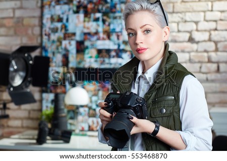 Portrait of attractive young female photographer holding camera, looking at camera.