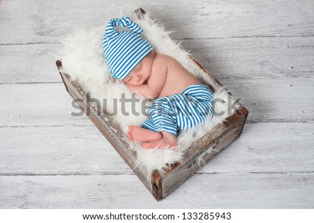 Newborn baby wearing blue and white striped pajamas and sleeping in a vintage, wooden, soda pop crate.