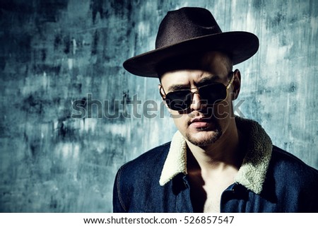Stylish brutal man wearing jeans clothes and sunglasses posing over grunge background. Denim collection. Male fashion.