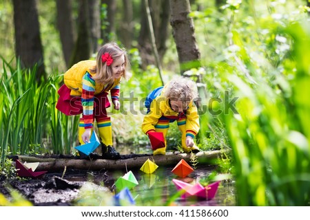 Children play with colorful paper boats in a small river on a sunny spring day. Kids playing exploring the nature. Brother and sister having fun at a forest stream. Boy and girl with toy boat and ship