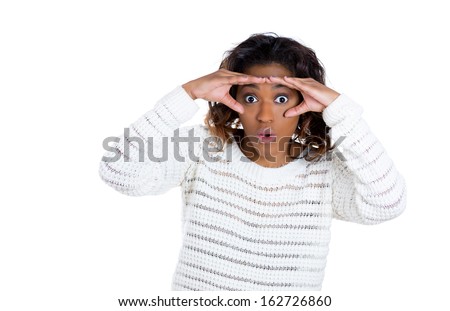 A closeup studio portrait of a young handsome, serious woman looking through her fingers like binoculars, searching for something, looking for the future at the camera, isolated on a white background