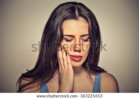 Closeup portrait young woman with sensitive toothache crown problem about to cry from pain touching outside mouth with hand isolated on gray background. Negative human emotion face expression feeling