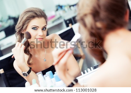 Reflection of young beautiful woman applying her make-up, looking in a mirror