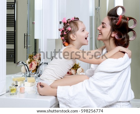 Young mother and daughter in curlers in a bath room happy smiling hugging each other family skin care concept in bathroom