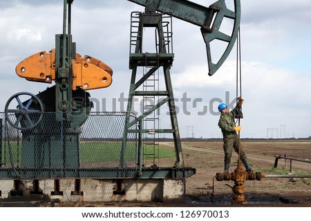 oil worker standing at pipeline and check pump jack