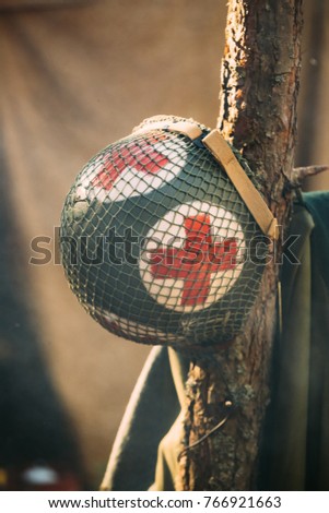 Metal Helmet Of United States Army Infantry Medic Soldier At World War II. Helmet Hanging On Tree Trunk In Forest Camp.