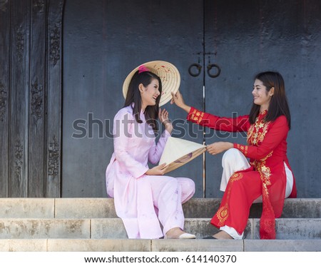 Two girls in ao dai Vietnamese's traditional costumes carry the hat sitting at the staircase in the ancient city