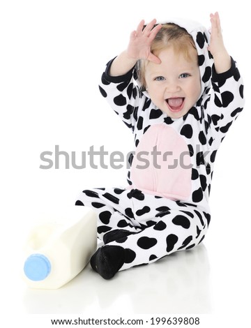 An adorable baby girl laughing excitedly in her holstein cow costume. She sits by a half gallon of milk. On a white background.