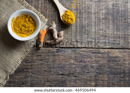 turmeric powder in spoon and roots on wooden table