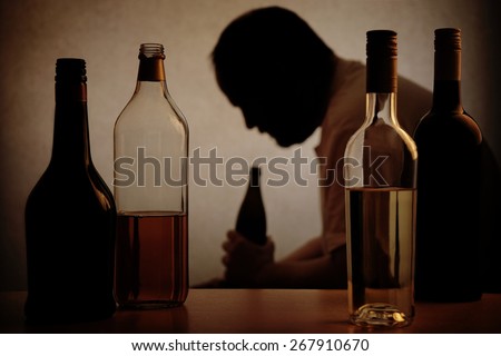 silhouette of a person drinking behind bottles of alcohol with added filter silhouette of a person drinking behind bottles of alcohol with added filter