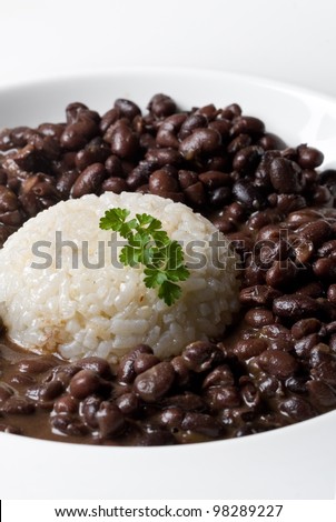 white rice accompanied by black dry beans served in a plate with parsley decoration. vertical composition