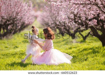 Mother with child girl playing in blooming spring garden. woman with daughter having fun outdoors in summer