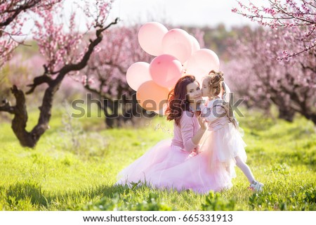 Mother with child girl playing in blooming spring garden. woman with daughter having fun outdoors in summer