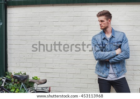 fashion man model, handsome male in casual jeans jacket near white brick wall on the street, background with place for text