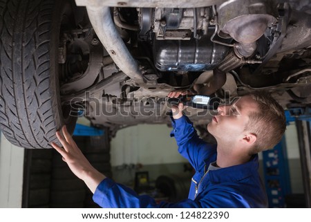Male mechanic examining car using flashlight