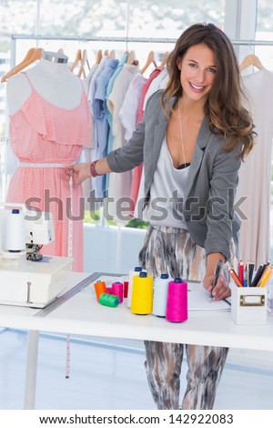 Fashion designer smiling to the camera and measuring dress on a mannequin