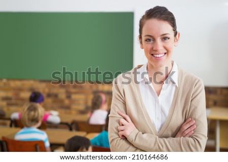 Pretty teacher smiling at camera at back of classroom at the elementary school