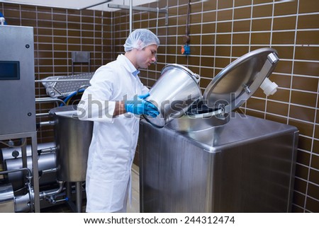 Smiling man in lab coat pouring something on the machine in the factory