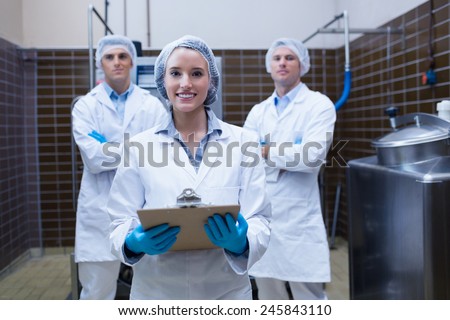 Girl holding a clipboard with these colleagues behind her in the factory