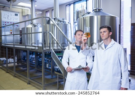 Two men in lab coat looking at the beaker with beer in the factory