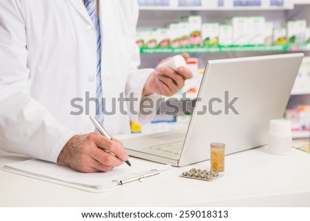 Pharmacist writing on clipboard and holding medication in the pharmacy