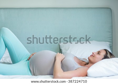 Pregnant woman lying on her bed in her bedroom