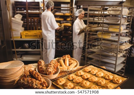Michetta and sweet food on a table while male and female baker working in background at bakery shop
