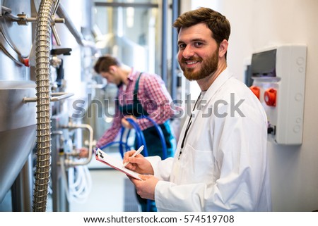 Portrait of maintenance workers examining brewery machine at brewery factory