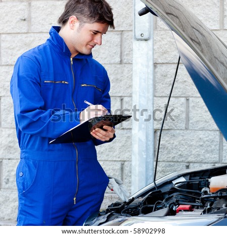 Handsome mechanic writing on a clipboard standing in front of a car