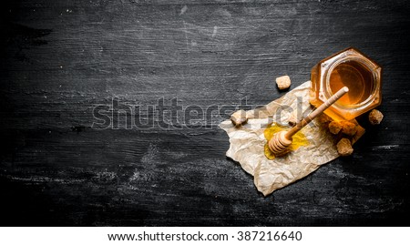 Natural honey with a spoon on old paper. On black rustic table.
