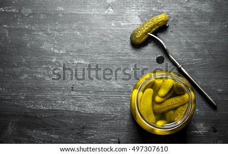 Pickled gherkins in a jar. On a black wooden background.