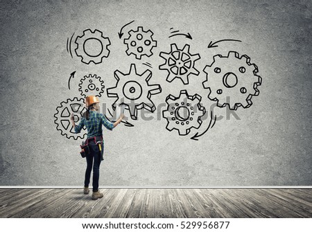 Back view of engineer woman in hardhat and sketched concept of teamwork on wall