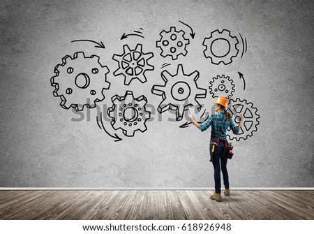 Back view of engineer woman in hardhat and sketched concept of teamwork on wall