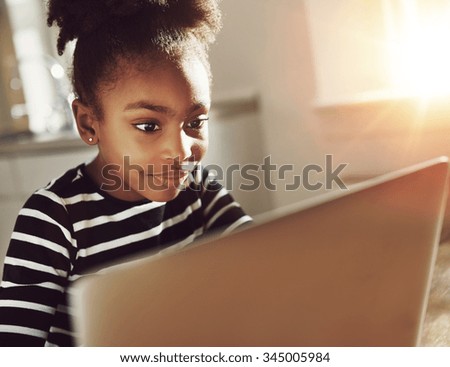 Smiling black girl using a laptop at home sitting reading information on the screen with an absorbed expression and a smile of pleasure