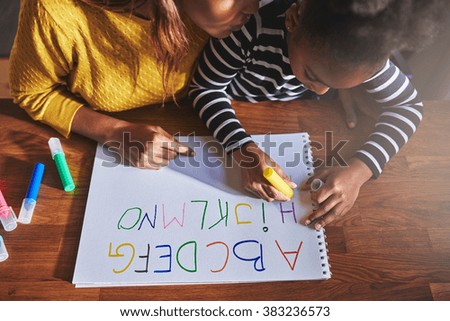 Overhead view of little girl learning the alphabet using coloured crayons