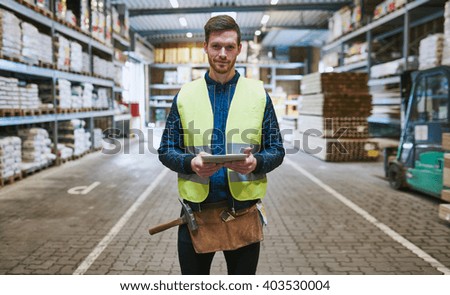 Young handyman or builder standing in the drive through in a hardware warehouse with a tablet in his hand looking at the camera