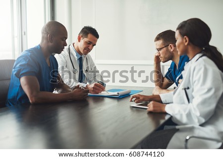 Multiracial medical team having a meeting with doctors in white lab coats and surgical scrubs seated at a table discussing a patients records